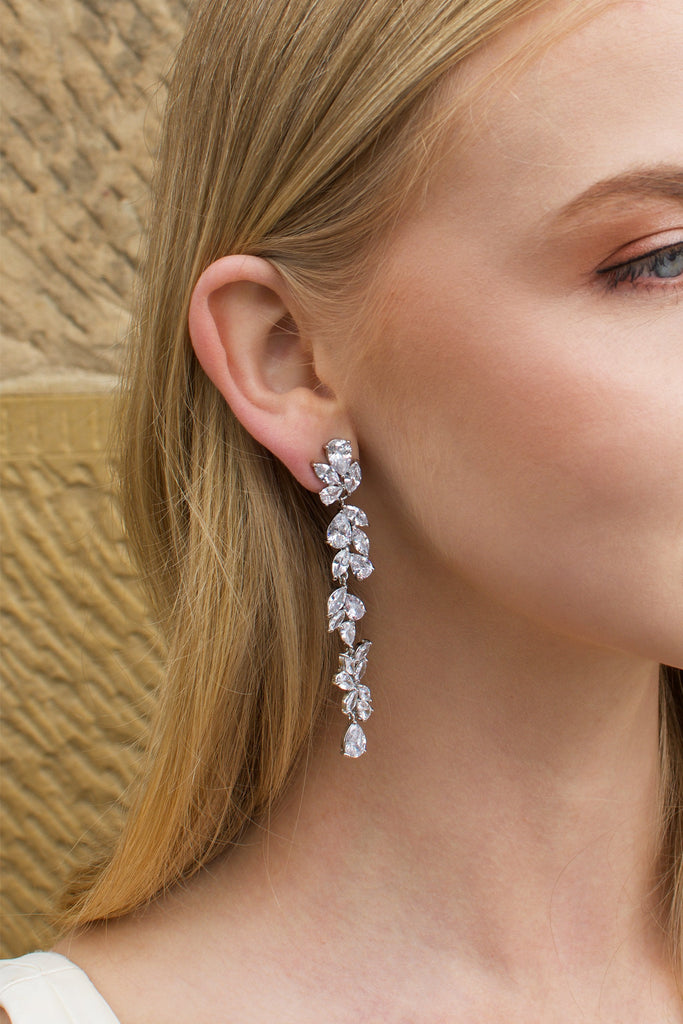 Long thin silver earring with stones worn by a blonde model with a sandstone wall backdrop