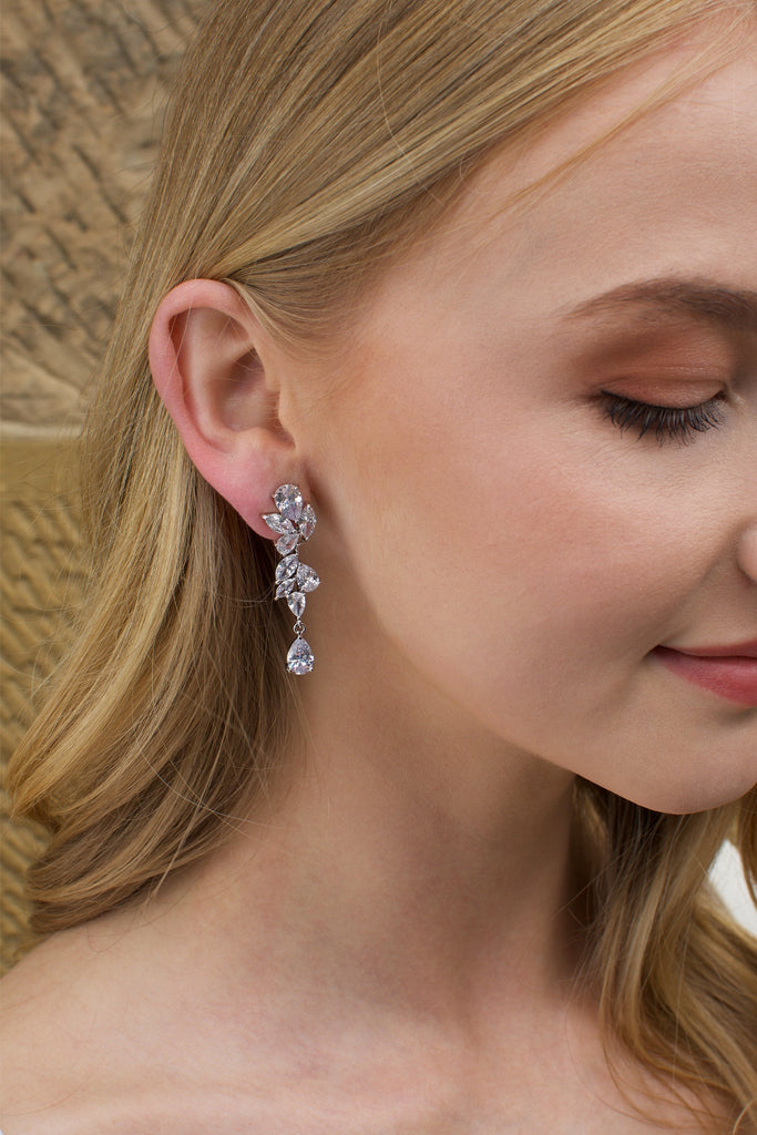 Blonde Model wearing a silver mid length earring with a stone wall backdrop