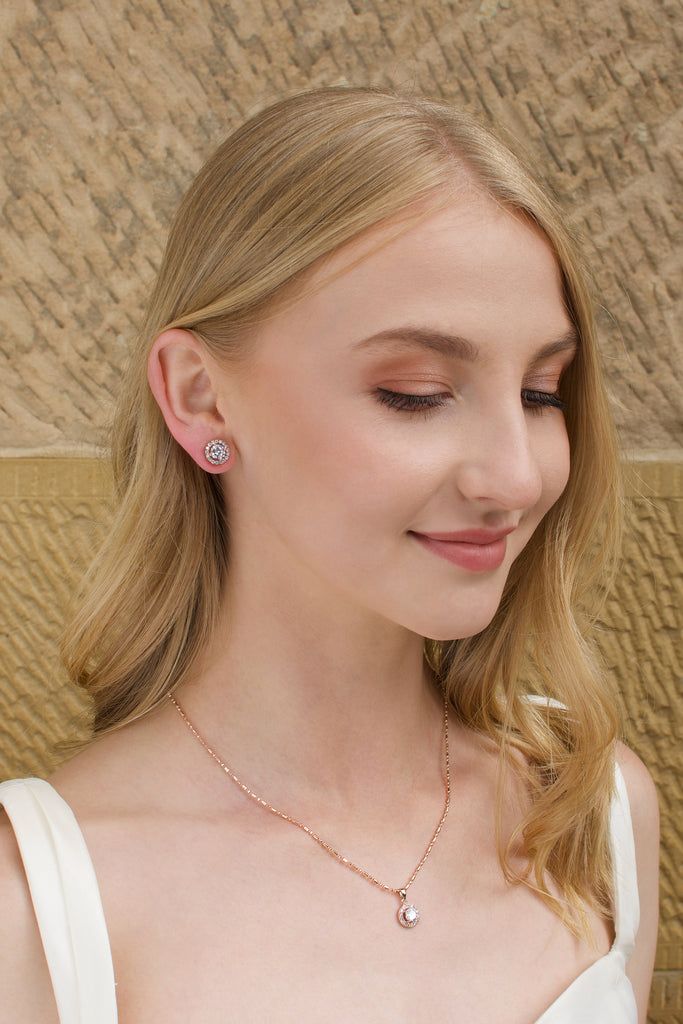 Model wears a simple rose gold chain with a single stone pendant with a stone wall background