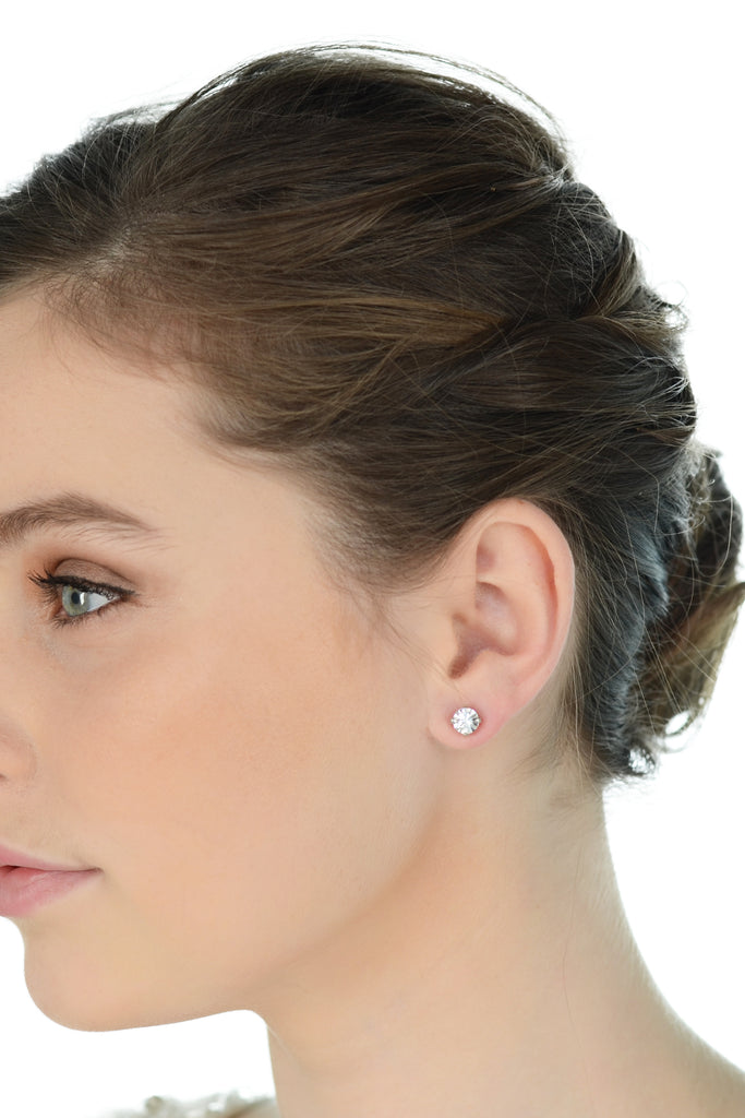A model with green eyes and dark hair looks away wearing a simple stud earring
