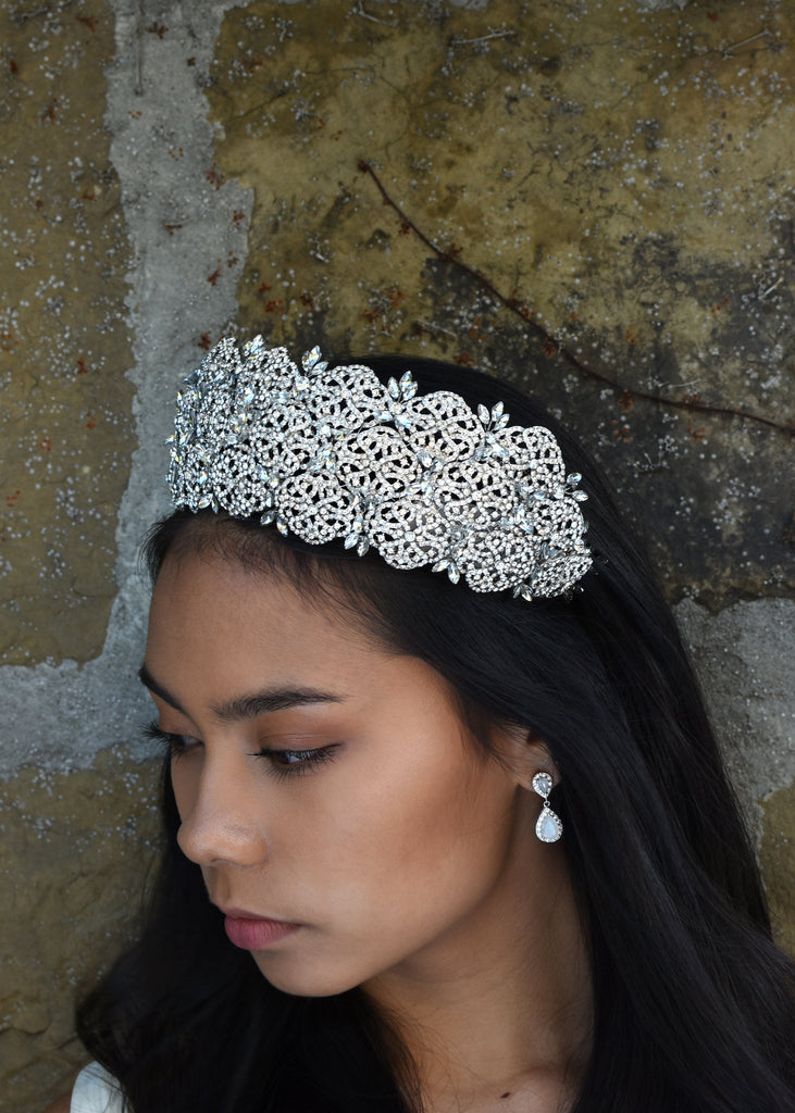 A very high crystal tiara worn by a dark haired bride with a stone wall behind her.