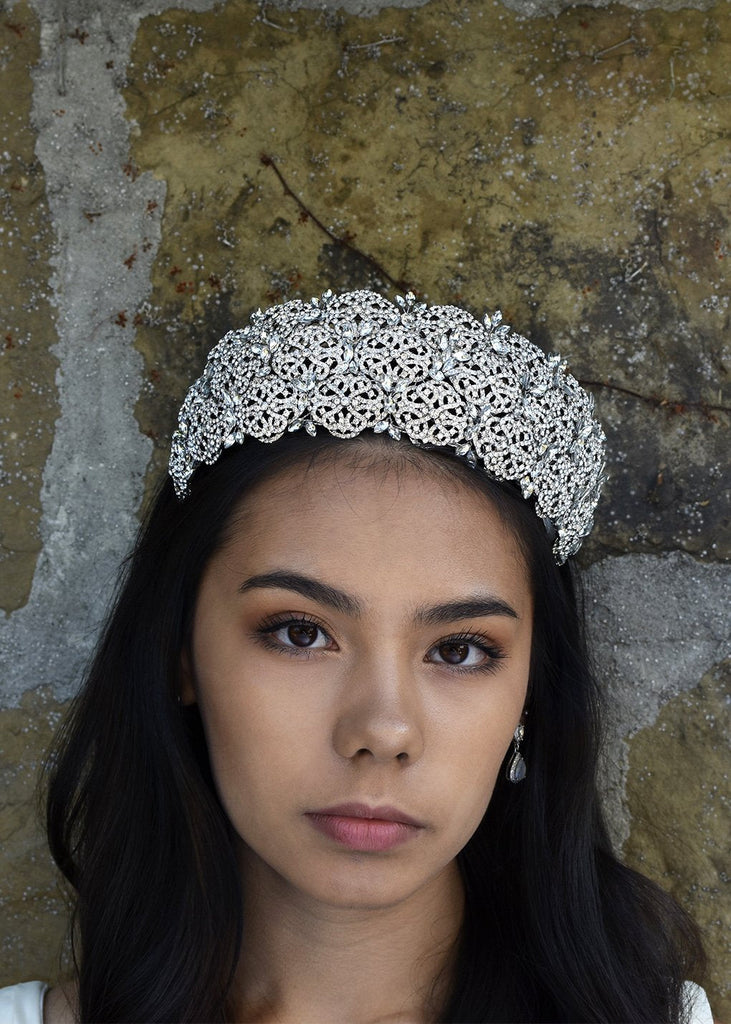 The front view of a bride wearing a high Bridal Tiara covered with tiny crystals with a stone wall background
