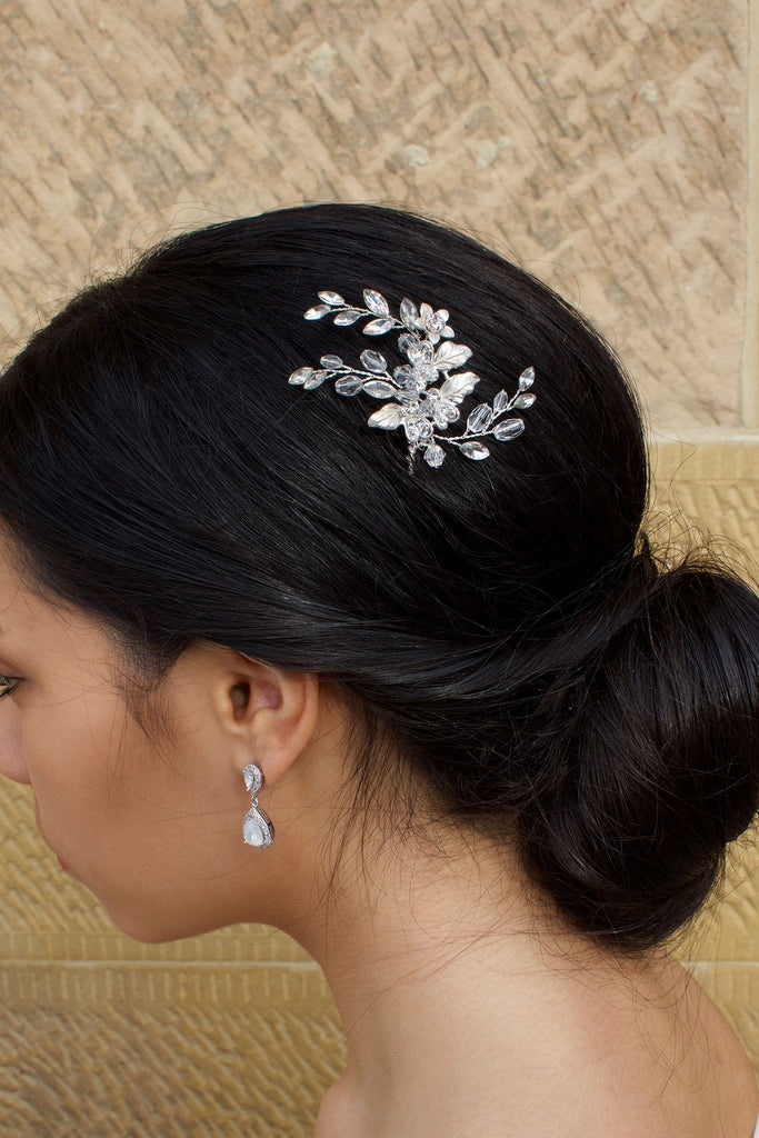 A model Bride with dark hair wears a small silver hairpin in her dark hair with a stone wall background