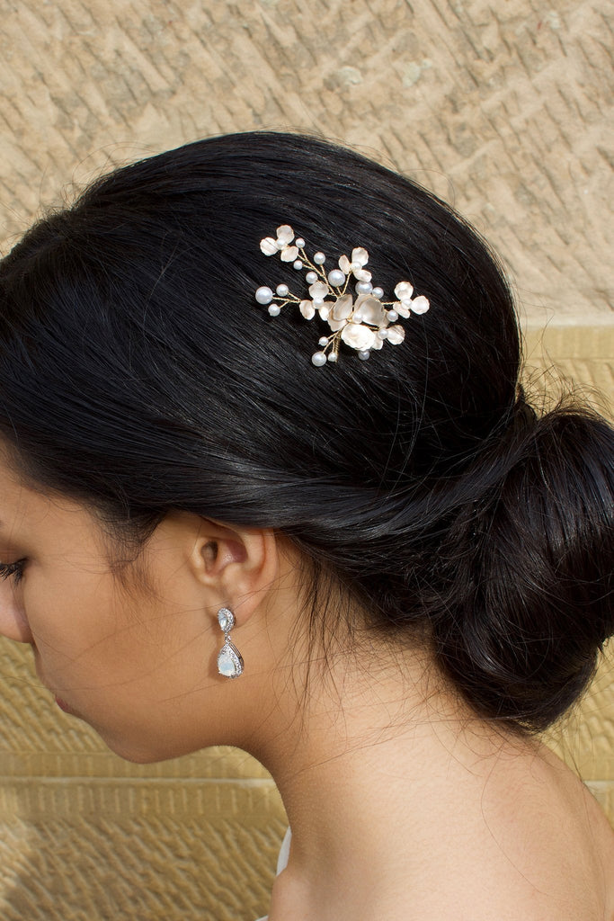Dark hair model wearing a small gold and pearl hair pin with a stone wall behind