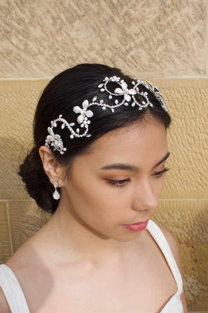 Dark Hair model wears a silver headband with pearls with a stone wall background