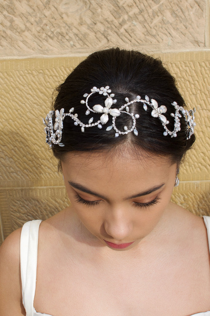 Head down model wears a silver bridal headband with pearls with a stone wall background