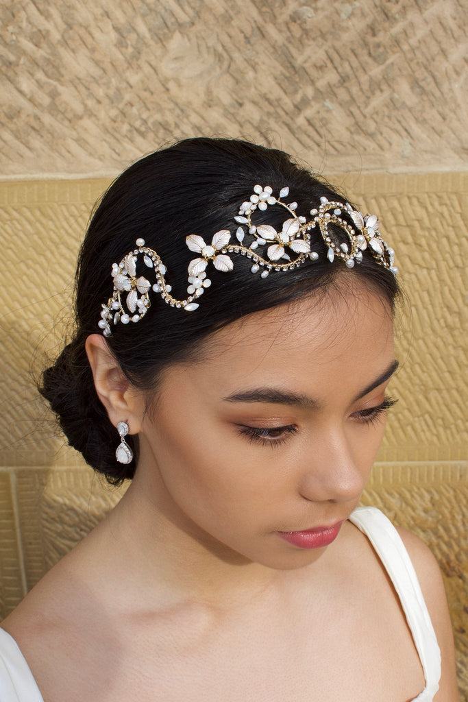 Black hair model wears a gold leaf headband. The model is standing in front of a sandstone wall.