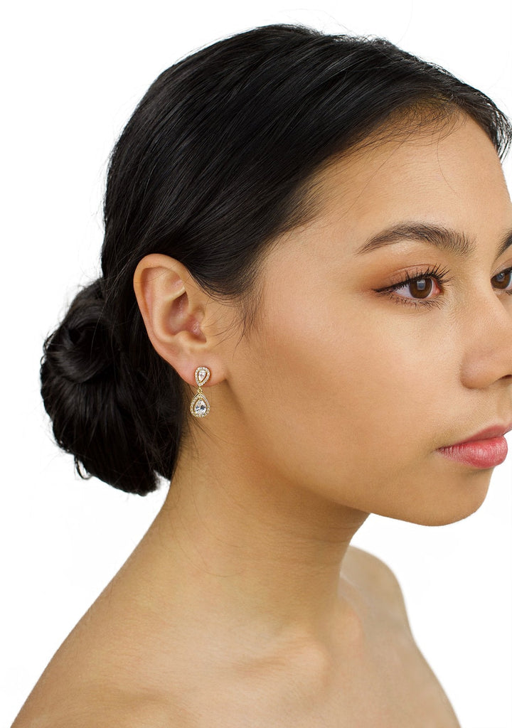 Very small gold drop earring worn by a dark hair bridal model with a white background