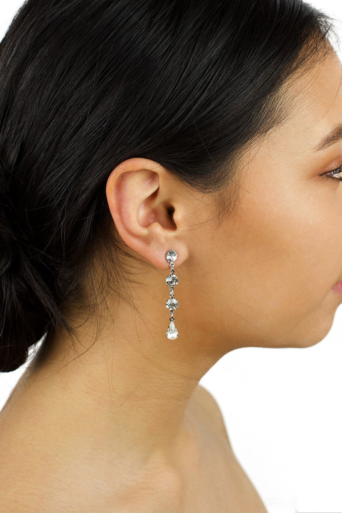 A dark hair model is wearing a long narrow earring in silver with clear stones