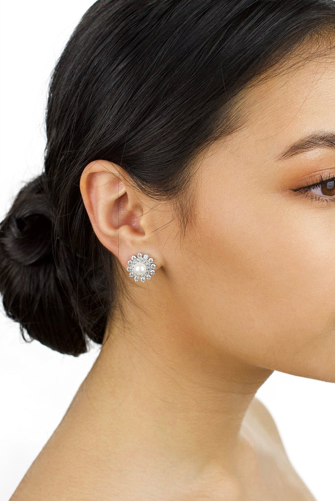 Model with dark hair up wears a stud earring of pearl and crystal with a white background