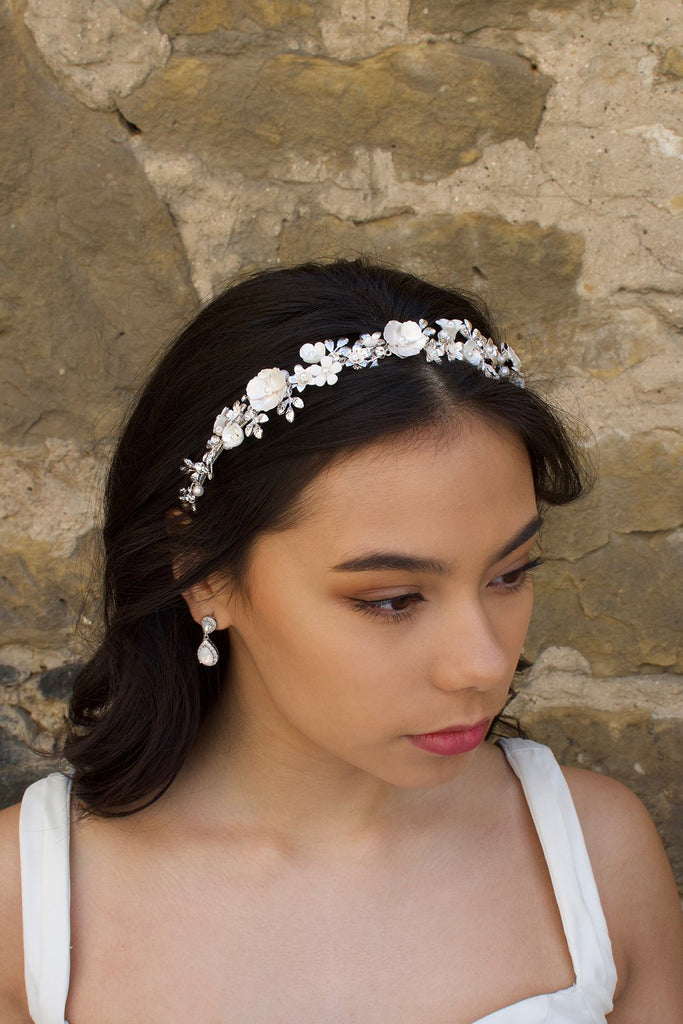 Brown Haired model wearing a ceramic flower headband in silver with a stone wall background