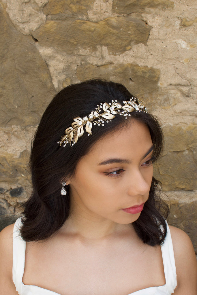 In front of a stone wall a dark hair Bride wears a soft gold bridal headband with tiny crystals
