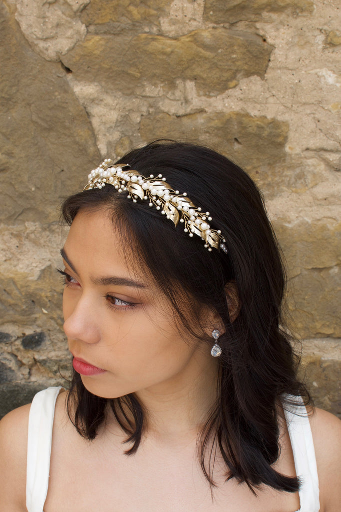 Looking away a model bride wears a pearls and pale gold headband on her dark hair