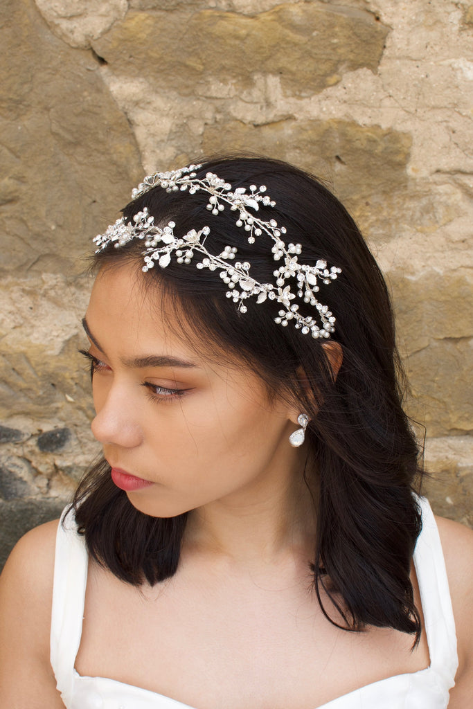 Silver double row headband on a black hair model with a pearl earring and a stone wall backdrop