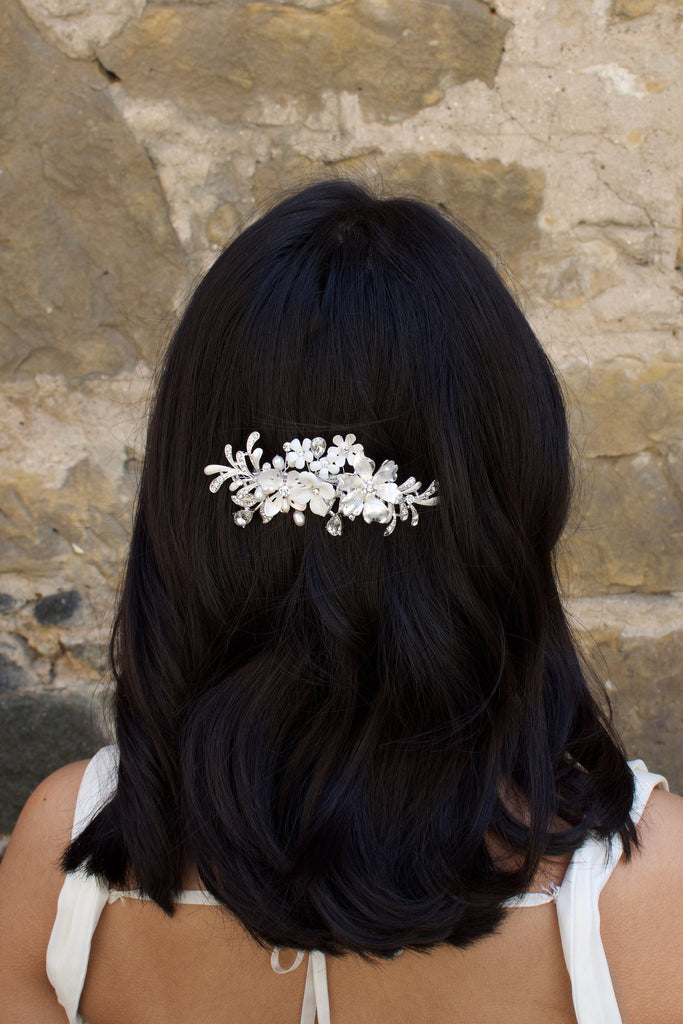 Model with dark hair wears a silver and flower side comb with a stone wall backdrop