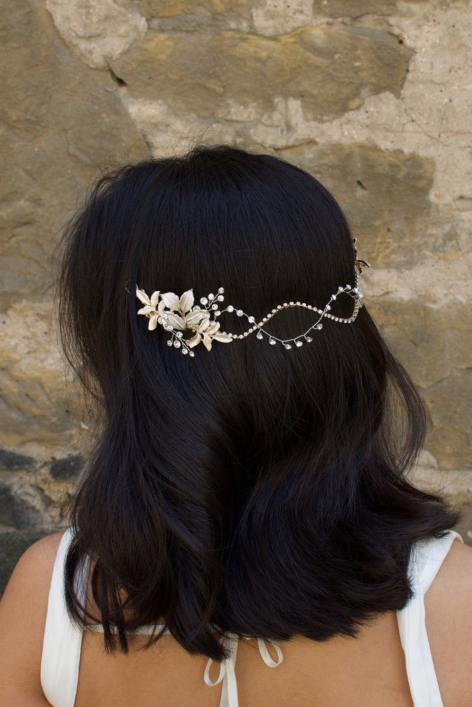 A Black haired model with her hair down wears a Silver soft bridal vine at the back of her head. Stone wall background