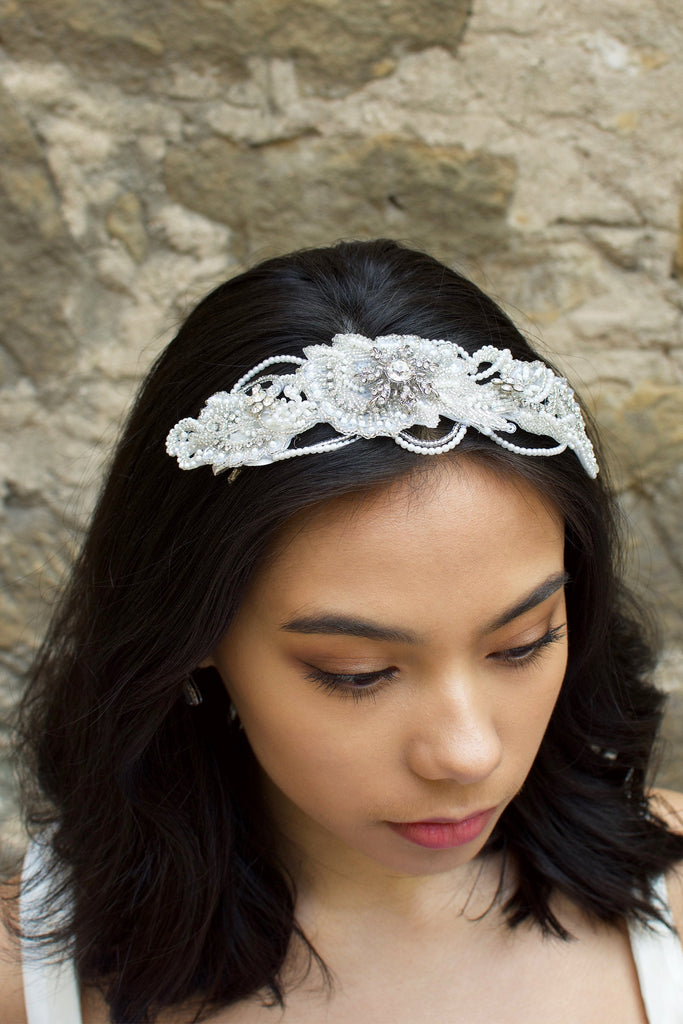 Dark Haired Bride wearing a seed pearl headpiece at the front on her black hair with a stone wall behind