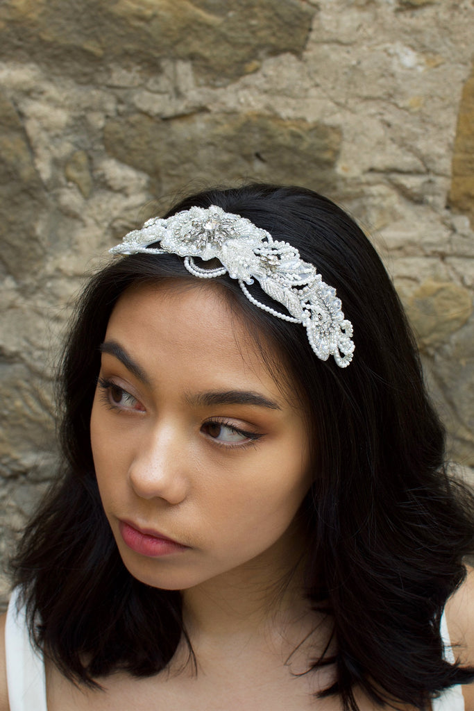 Bride with black hair wearing a seed pearl bridal comb at the front of her head with a stone wall background