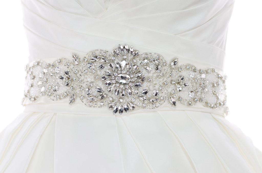 A wide bridal belt with crystals and beads worn on the waist of an ivory bridal gown with a white background