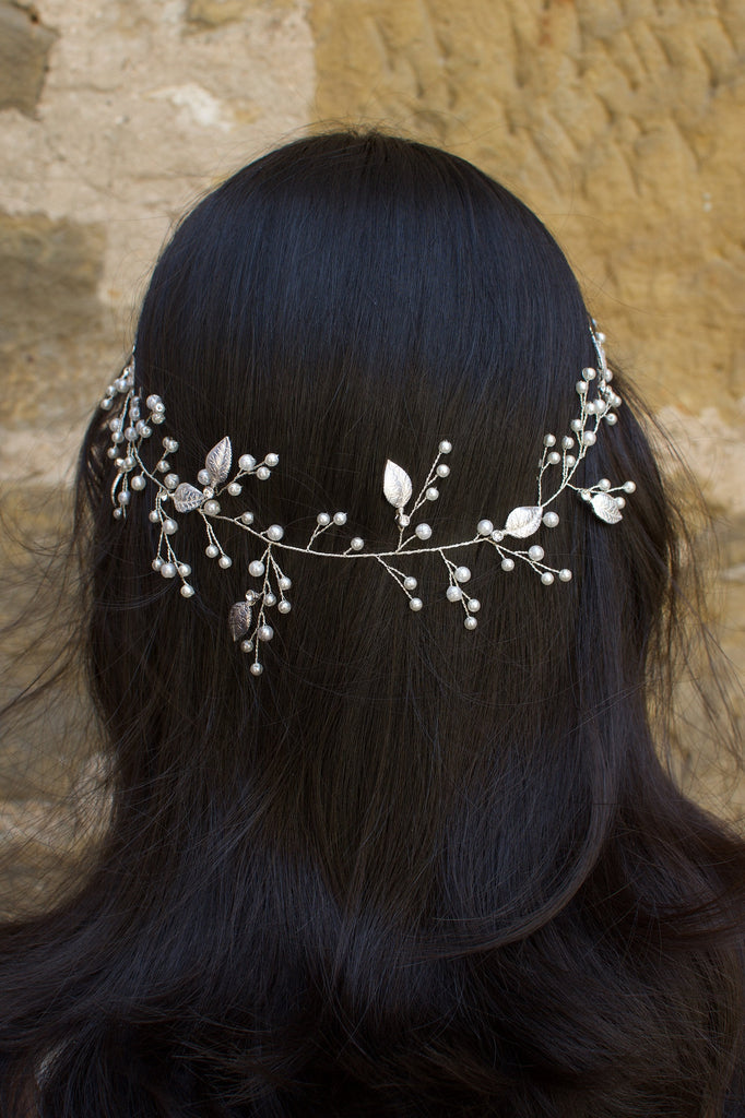 A silver pearl bridal vine with leaves worn by a dark haired model on the back of her head