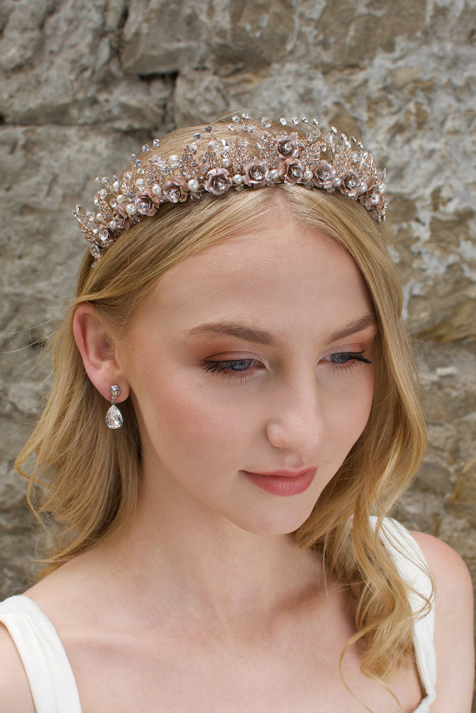 A Rose Gold Flowers and pearls wide tiara worn by a blonde bride with a stone wall background.
