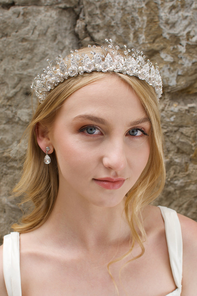 A Soft Silver Flowers and pearls wide tiara worn by a blonde bride with a stone wall background.