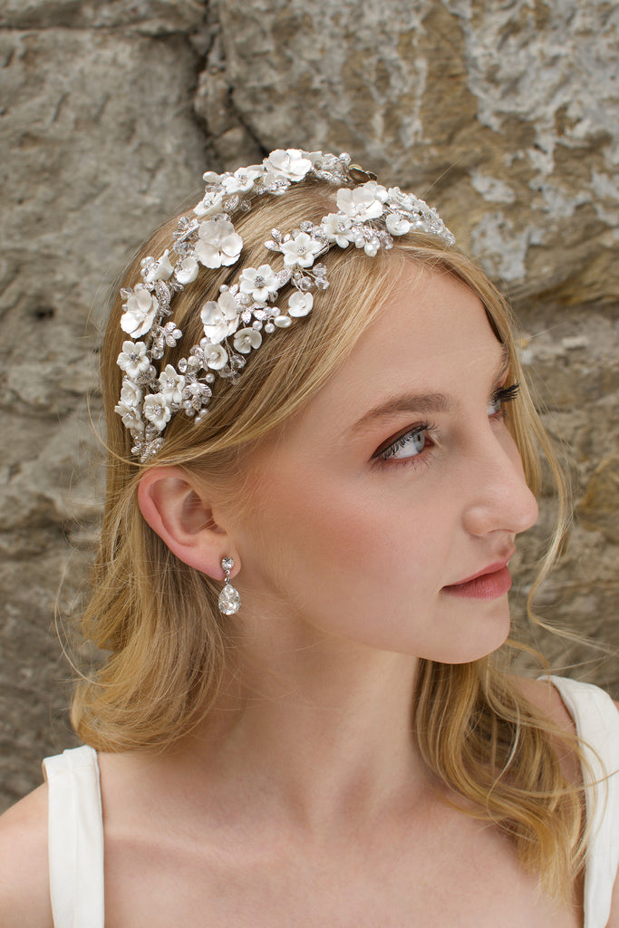 Blonde model looks up wearing a 2 row flowers headband with a stone backdrop
