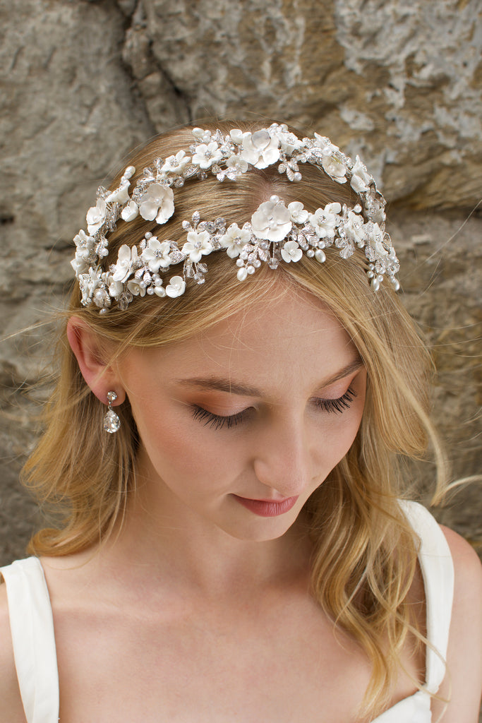 Blonde hair model looks down wearing a twin row bridal headband of flowers with a stone background