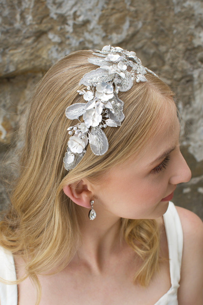 Bridal headband with Lace leaves and white flowers worn by a blonde bride in front of a stone wall. 