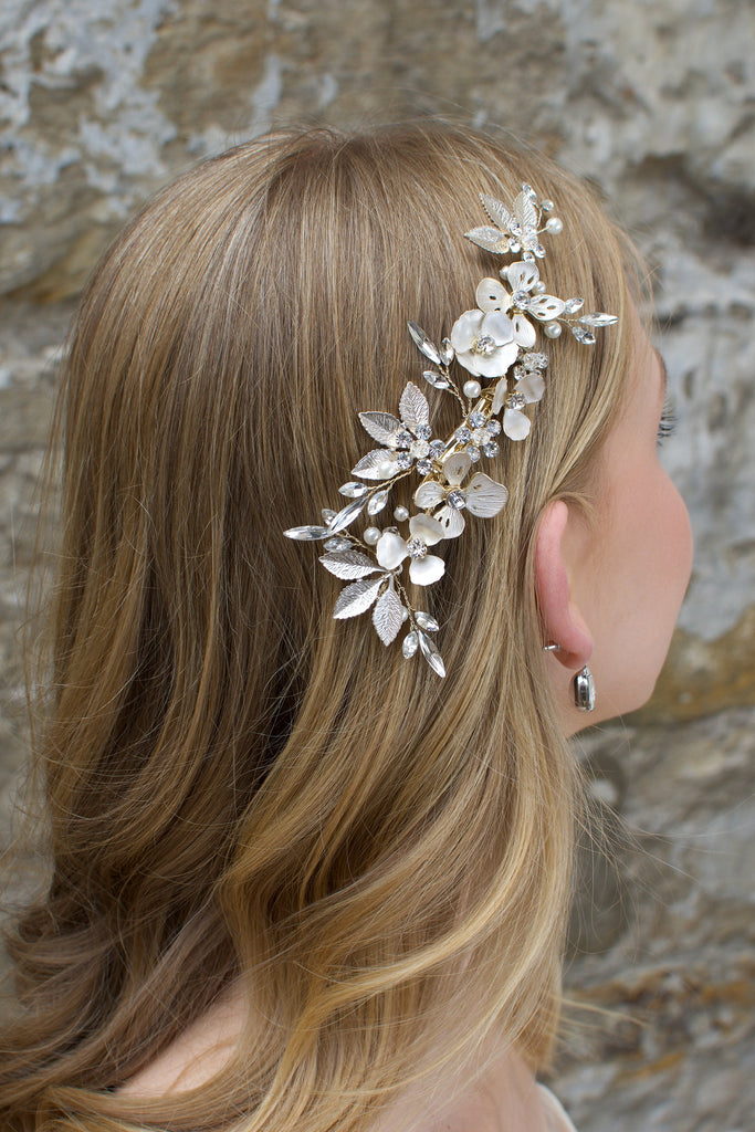 A Comb with different flowers and leaves in Pale Gold with pearls sits on the head of a blonde model bride