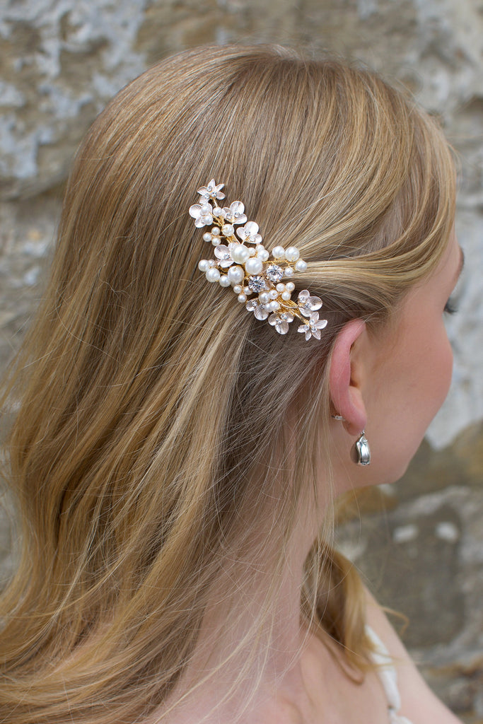 Blonde hair model wears a pearl hair clip in gold in front of an old stone wall