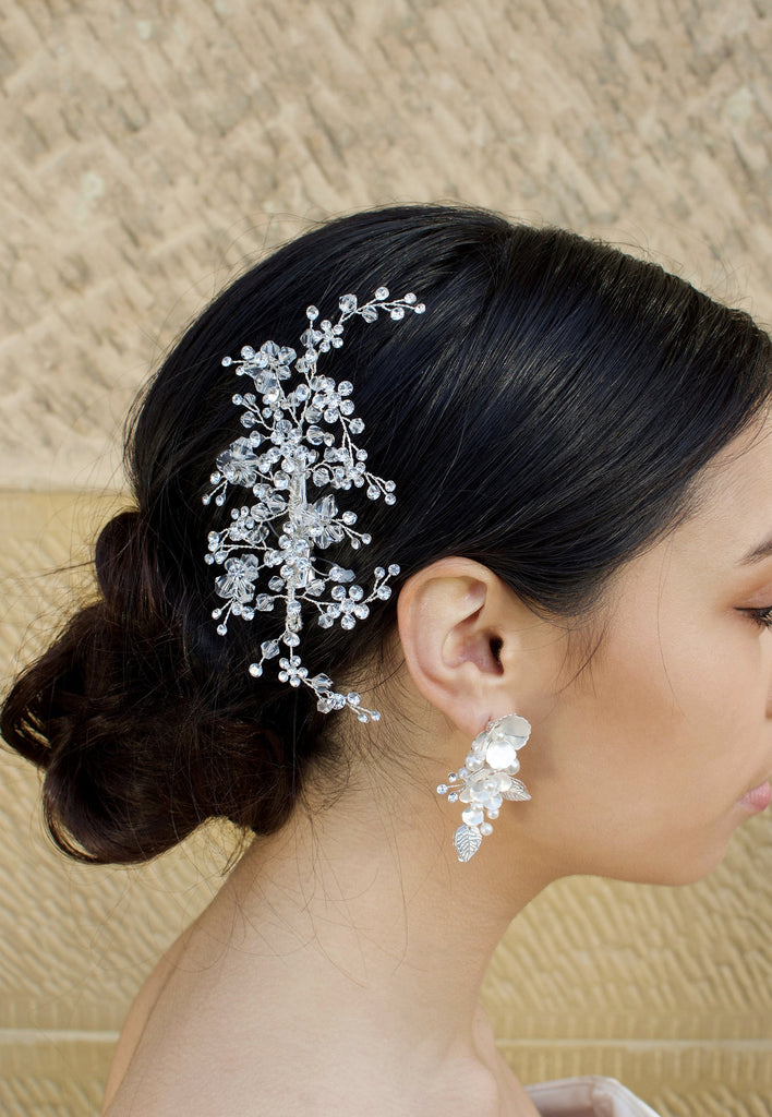 Clear Crystals headpiece on the side of a dark hair model wearing a white flower earring with a stone wall background