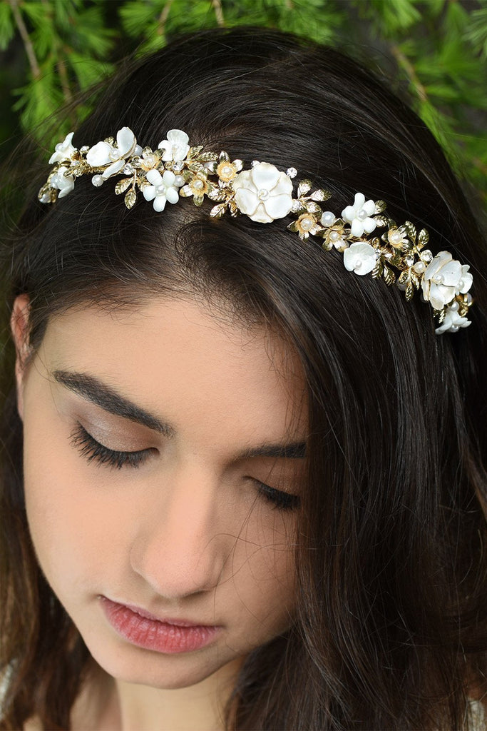 White Flowers and gold leaves headband worn at the front of a dark hair model's head with pine tree background