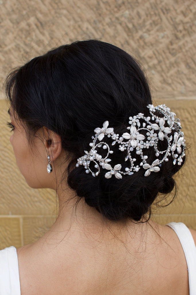 Dark hair model wears a Silver Bridal Headpiece over a large bun of hair with a stone wall background