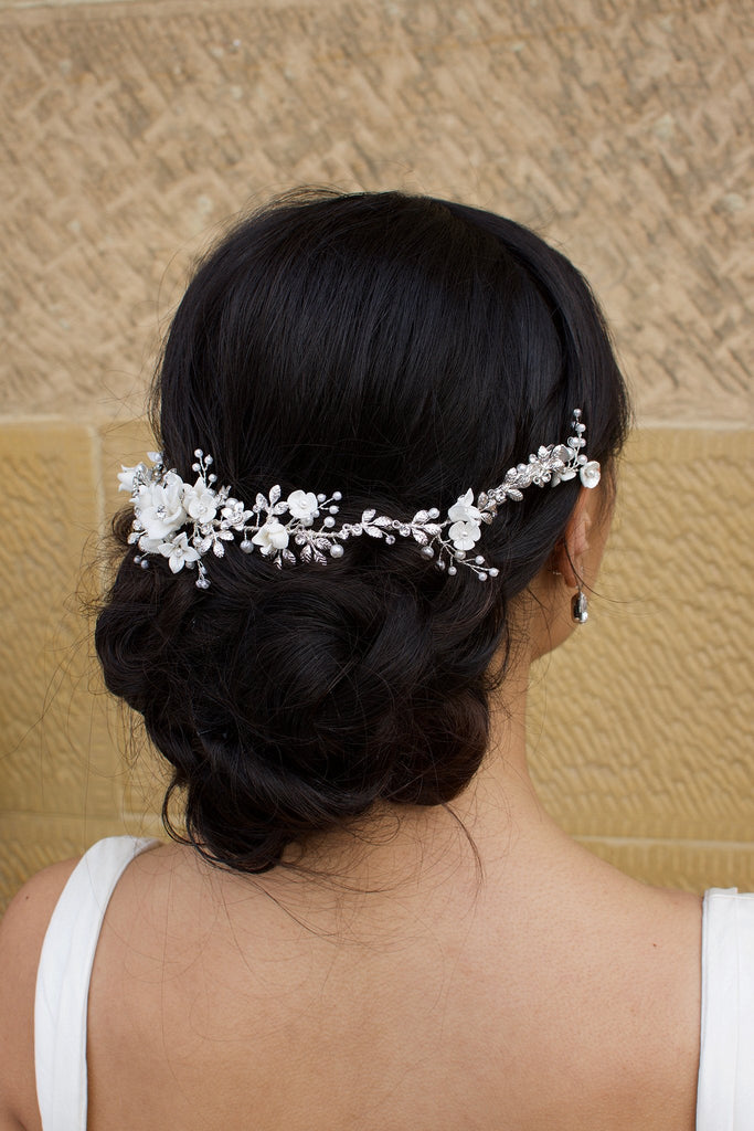 A black haired Bride wears a porcelain flowers silver vine around the back of her head with a stone backdrop