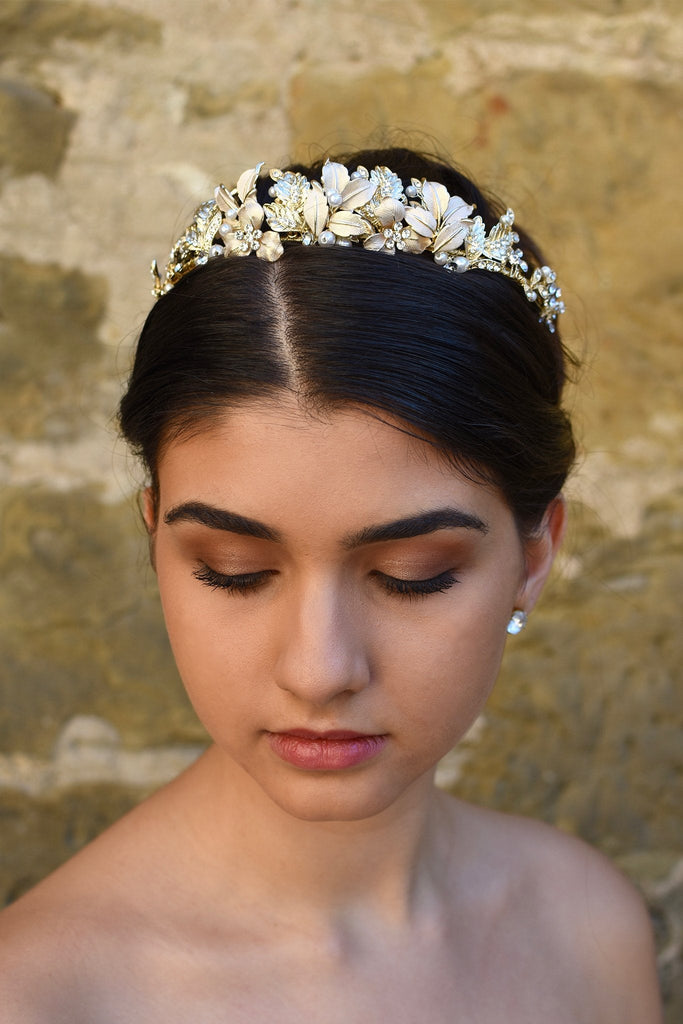 A dark haired model wears a pale gold low tiara with leaves and flowers