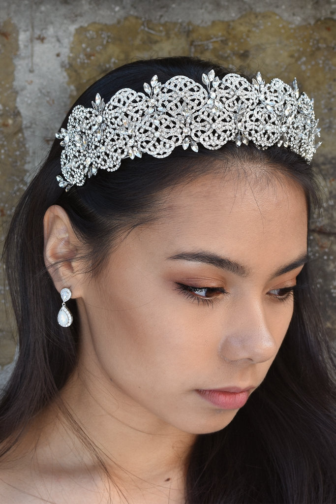 A wide crystal crown is worn by a dark haired model standing in front of a stone wall