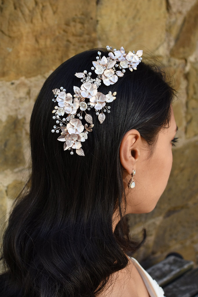 A Dark haired model wears a long Pale gold side comb with flowers and a small earring