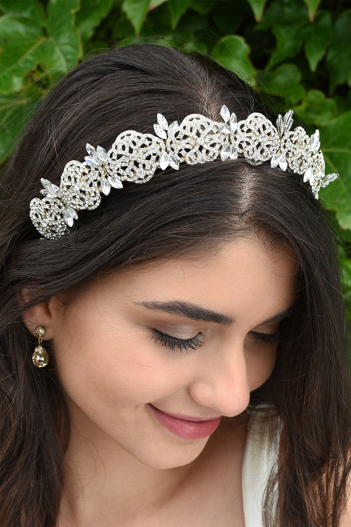 Smiling Bride looks down wearing a gold bridal headband full of tiny crystals with a background of leaves