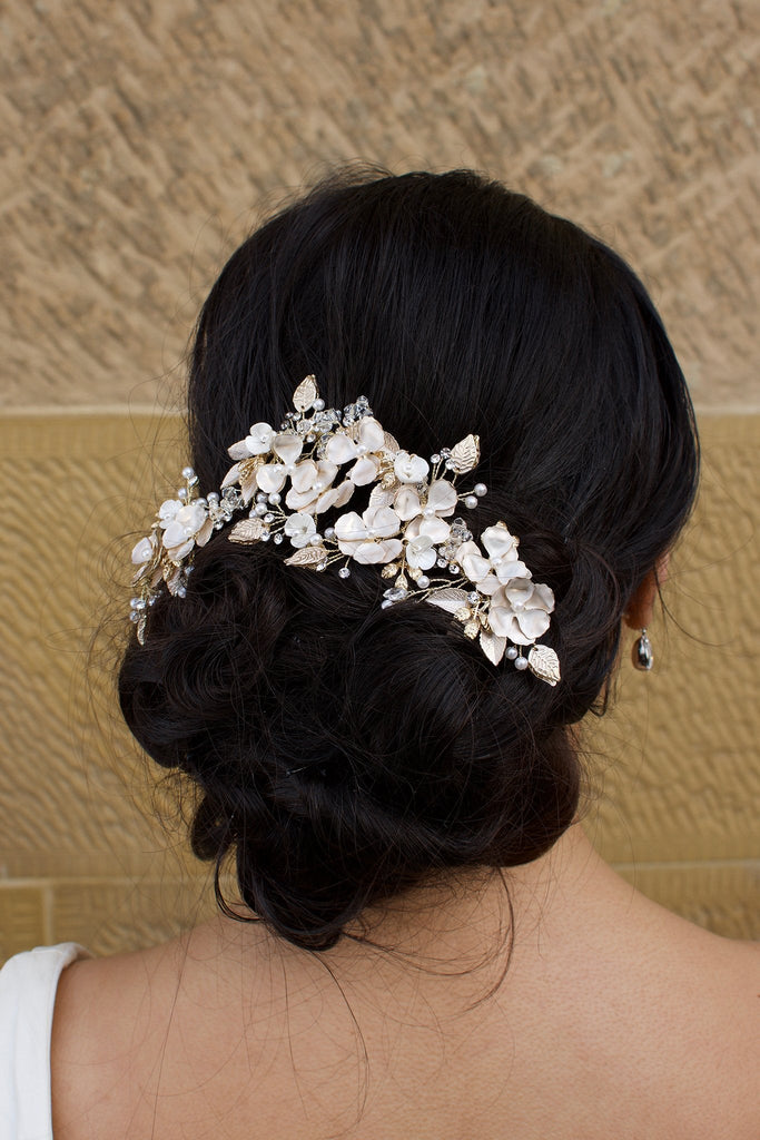 A dark haired bride wears a gold flowers headpiece at the back of her head with a stone wall background