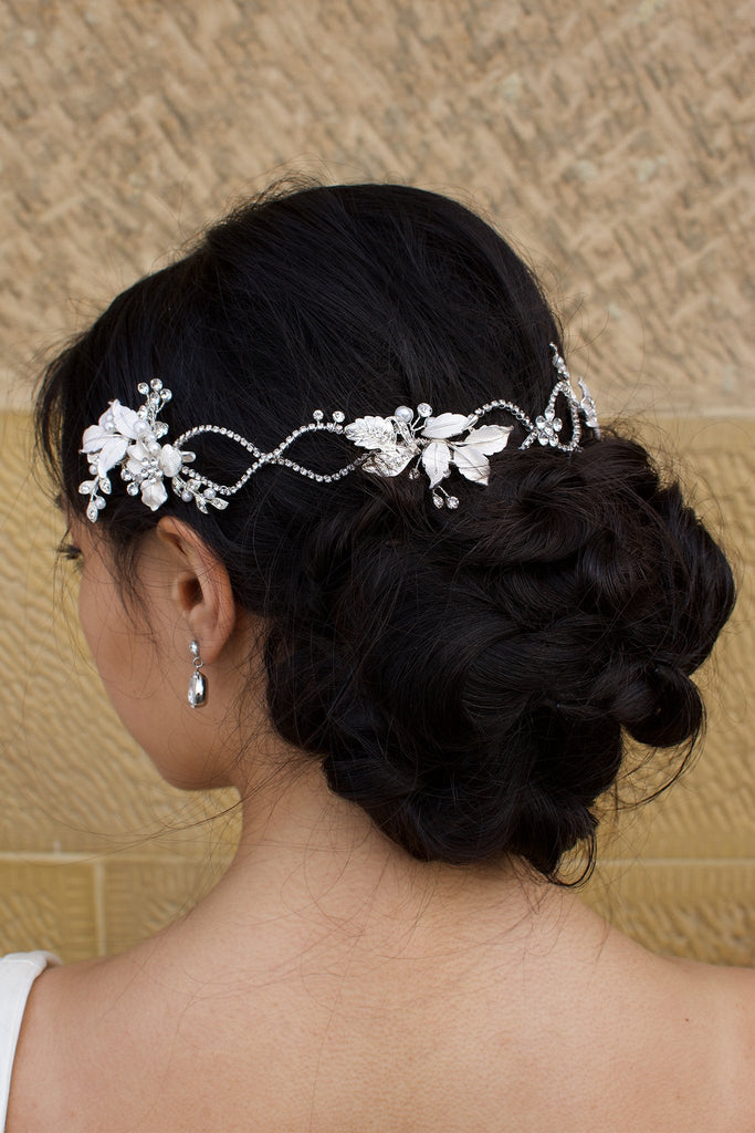 A dark haired model with curly hair wears a silver vine at the back of her head