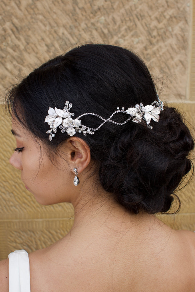 A dark haired model with curly hair wears a silver vine at the back of her head with stone background